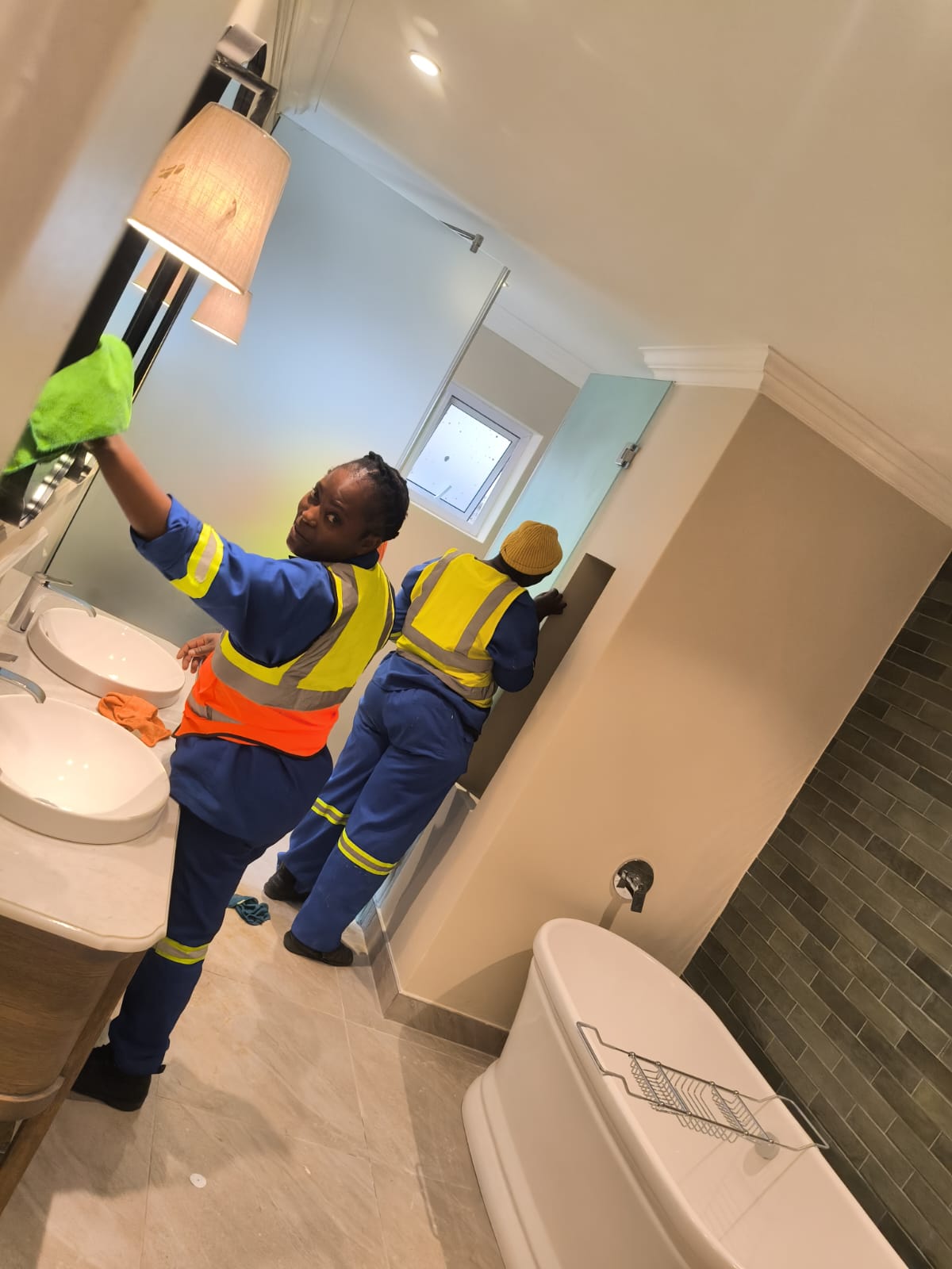 Two cleaners wiping mirrors and walls in a bathroom