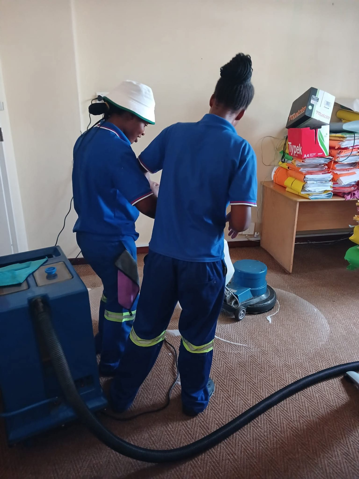 Two cleaners scrubbing an office carpet with a rotary machine