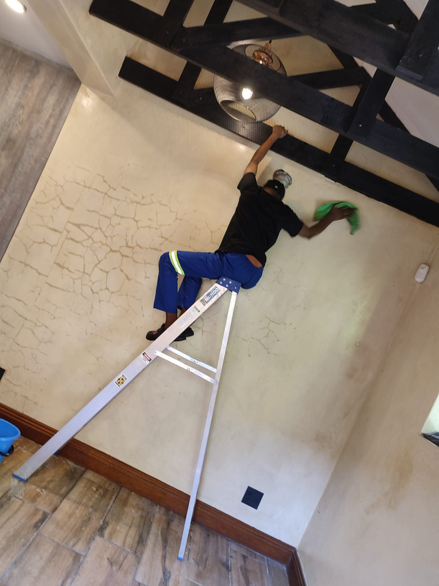 Cleaner on a ladder wiping a high wall near ceiling beams