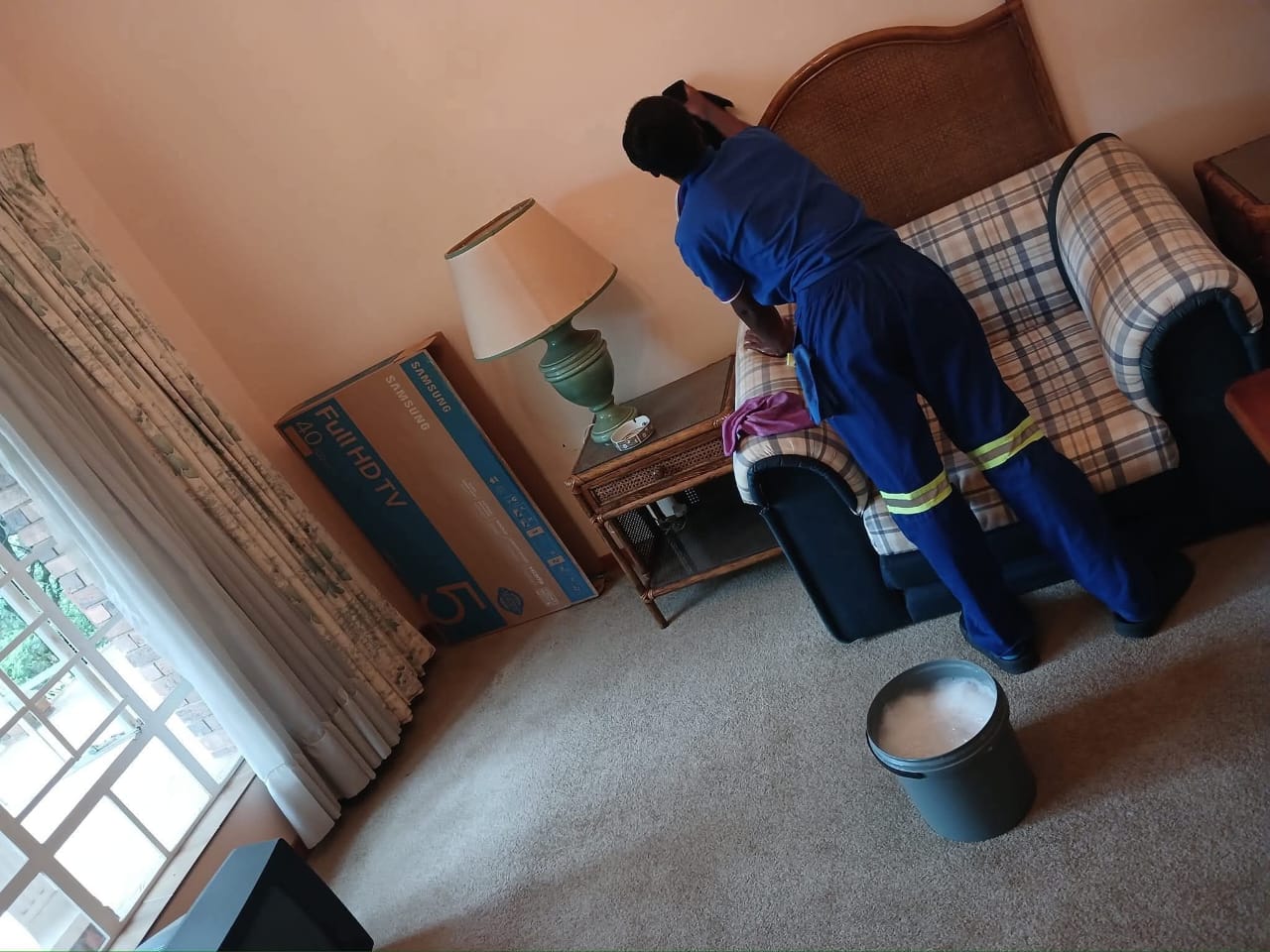 Cleaner in a blue uniform working on a patterned couch