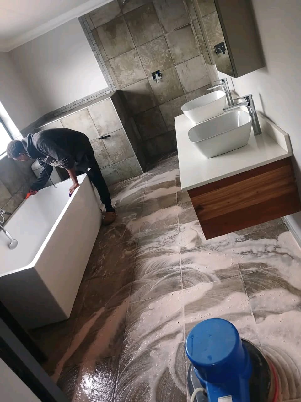 Rotary scrubber foaming a bathroom floor while a cleaner wipes the bath